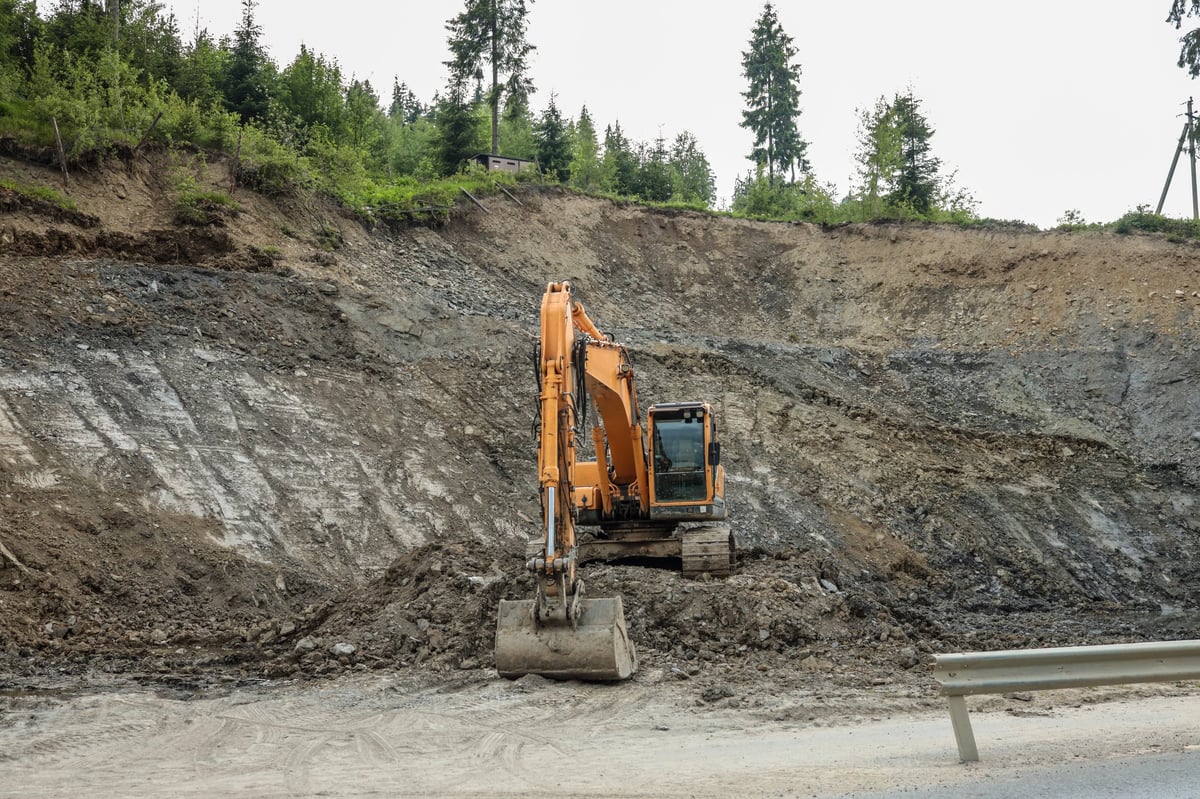 Excavator working near a road on a rocky slope