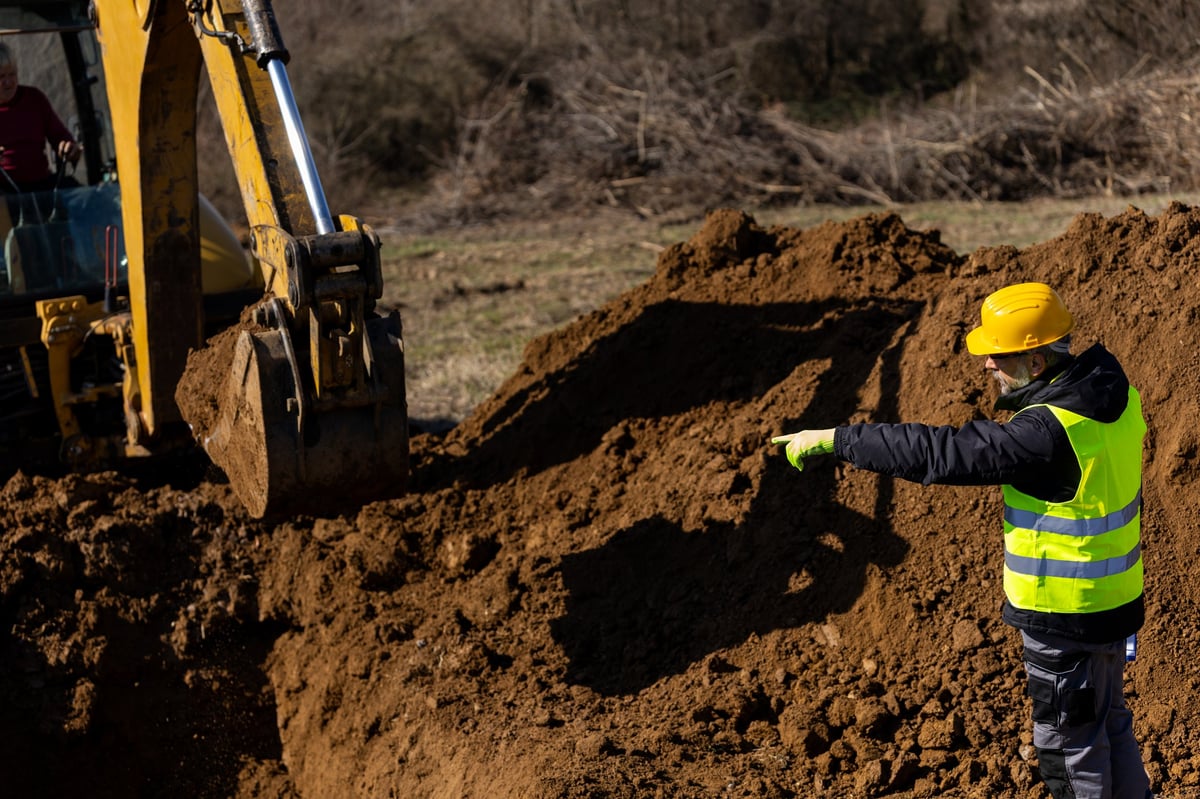Construction worker guiding an excavator bucket during earthmoving